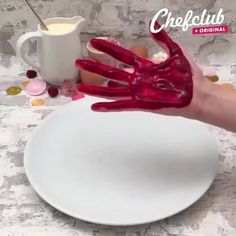 a person's hand covered in red paint on top of a white plate next to a cup