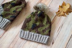 two knitted hats sitting on top of a wooden floor next to an autumn leaf