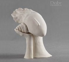 a white ceramic sculpture of a woman's head with her hands in her hair