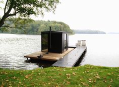 there is a small boathouse on the water with two chairs in front of it