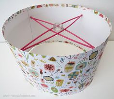 a white lamp shade with colorful flowers on it and red string hanging from the bottom