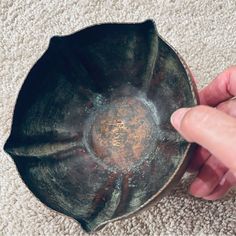 a hand is pointing at an old metal bowl