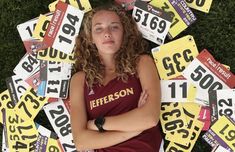 a woman standing in front of a pile of license plates with her arms crossed and looking at the camera