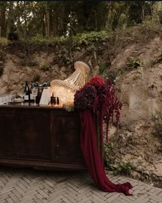 a wooden table topped with bottles of wine next to a hill covered in dirt and grass