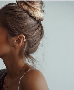 a woman with her hair in a high bun, looking down at the camera and wearing earrings