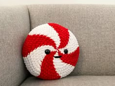 a red and white knitted ball sitting on top of a gray couch next to a pillow