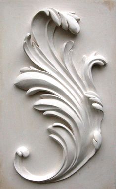 a white decorative design on the side of a building's wall, with swirls and leaves carved into it