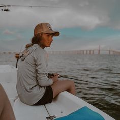 a woman sitting on the back of a boat while holding a fishing rod in her hand