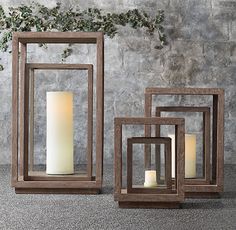 three wooden frames with candles in them sitting on the ground next to a stone wall