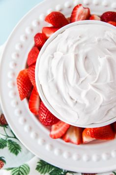 a white plate topped with whipped cream and strawberries on top of a floral table cloth