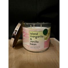 a candle that is on top of a wooden table next to a container with the label island margarita and vanilla bean