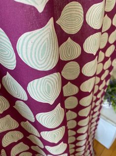 a purple and white curtain hanging from a wooden floor next to a potted plant