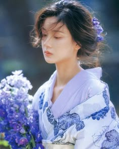 a woman in a blue and white kimono holding purple flowers