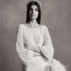 a woman in a white dress with feathers on her head and arms crossed, wearing a tiara