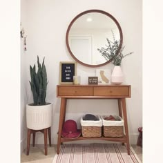 a wooden table with baskets under a round mirror on top of it next to a potted plant