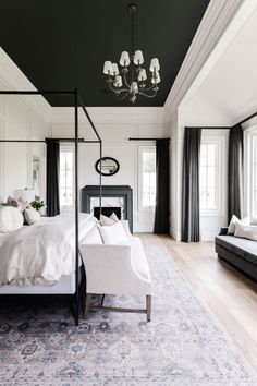 a bedroom with black and white walls, a canopy bed, chandelier, two couches and windows