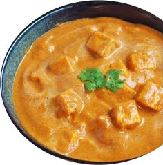 a bowl filled with curry and tofu on top of a wooden table next to rice