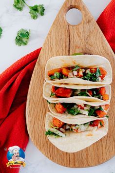 three tacos sitting on top of a wooden cutting board next to a red towel