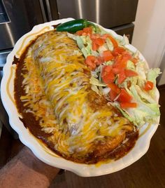 a white plate topped with a taco covered in cheese and lettuce next to a salad