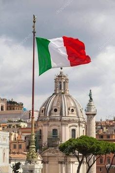 an italian flag flying in front of the dome of a building with other buildings behind it