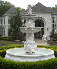 a fountain in front of a house with hedges around it and bushes surrounding the building