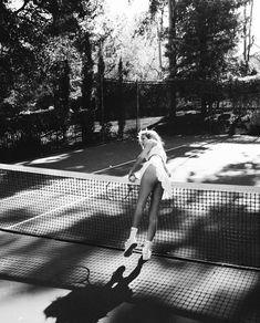 a black and white photo of a woman playing tennis on a court with trees in the background