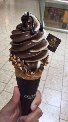 a person holding up an ice cream cone with chocolate and nuts on top in front of a tiled floor