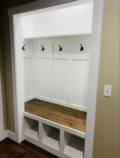 an empty white bench with three hooks on it's back and two coats hanging from the wall