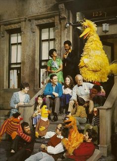 a group of people sitting on the steps in front of a building with a large yellow bird