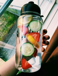 a person holding a glass jar filled with fruit and veggies