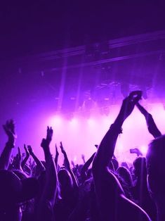 a crowd of people at a concert with their hands in the air and lights on