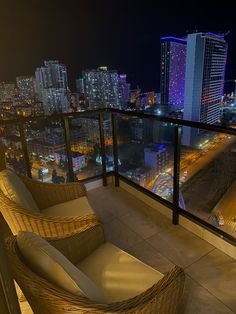 two wicker chairs sitting on top of a balcony next to a cityscape