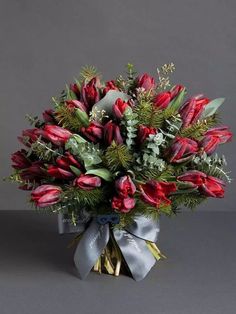 a bouquet of red tulips and greenery in a glass vase on a gray background