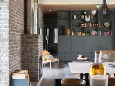 a living room filled with furniture next to a fire place and bookshelf in front of a brick wall