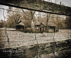 an old abandoned house in the middle of a field behind a fence with barbed wire