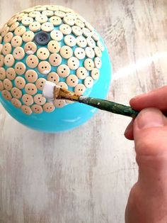 a person holding a paintbrush in their left hand and painting the inside of a ball with buttons on it