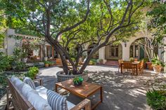 an outdoor seating area with tables and chairs under a tree in front of a house