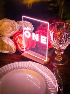 there is a light up sign on the table with wine glasses and flowers behind it