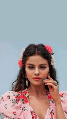 a woman in a pink floral dress holding a cell phone to her ear and looking at the camera