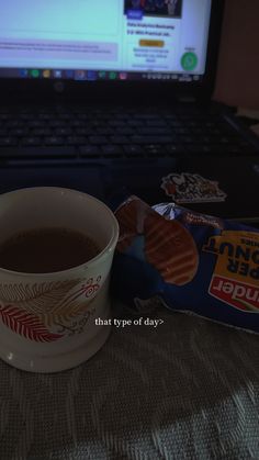 a cup of coffee next to a bag of chips and a laptop on a bed