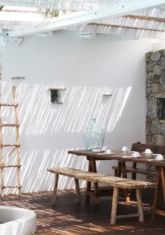 a wooden table sitting under a glass roof next to a white wall with windows on it