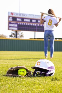 a softball helmet and catchers mitt sitting on the grass in front of a scoreboard