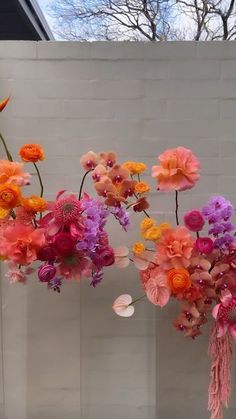 three vases with flowers hanging from them in front of a brick wall and tree