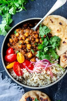 a bowl filled with rice, beans and vegetables next to pita bread on a blue surface