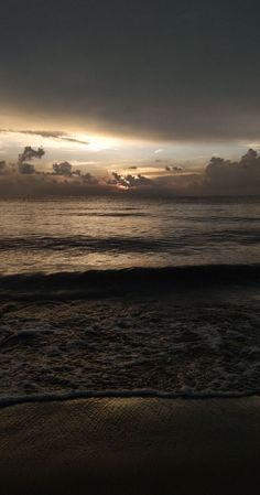 the sun is setting over the ocean with clouds in the sky and waves on the beach