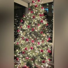 a white christmas tree with red ornaments and lights in front of a window at night