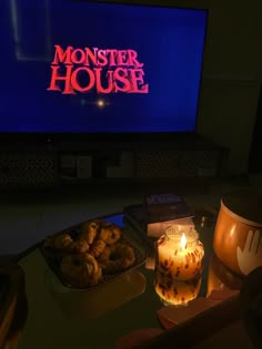 a table with some food and a candle in front of a television screen that reads monster house