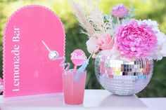 a table topped with a vase filled with flowers next to a mirror ball and drink