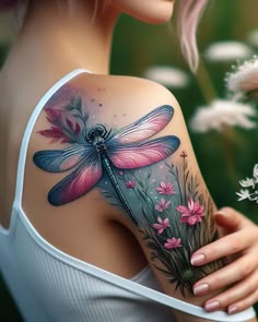 a woman's shoulder with a dragonfly tattoo on her arm and flowers in the foreground