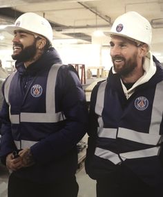 two men in hard hats standing next to each other at an assembly line, smiling